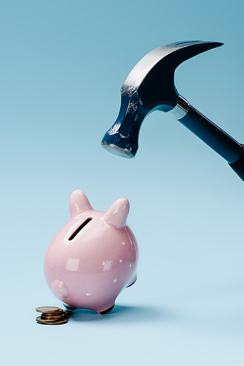 close up view of pink piggy bank with stack of coins and hammer isolated on blue