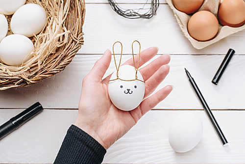 cropped image of woman holding chicken easter egg with bunny ears and smiley above table
