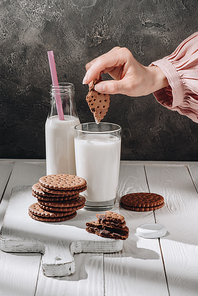 cropped shot of woman dipping chocolate cookie into glass of milk