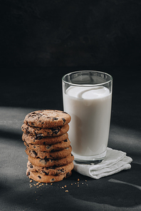 stack of chocolate-chip cookies with glass of milk on black surface