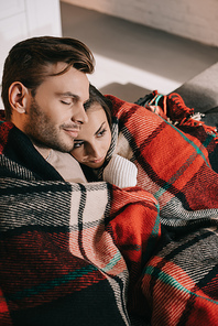 high angle view of happy young couple relaxing on couch and covering with plaid