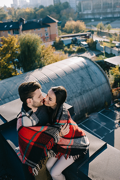 high angle view of happy young couple covered in plaid kissing on rooftop