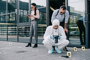 male detective viewing photos of crime scene with male criminlogist while female detective making notes