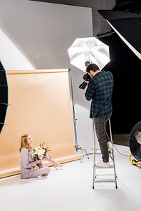 photographer standing on step ladder and shooting beautiful girl with flowers in studio