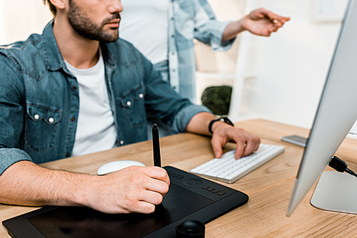 cropped shot of male retoucher using drawing tablet while workign with colleague in office