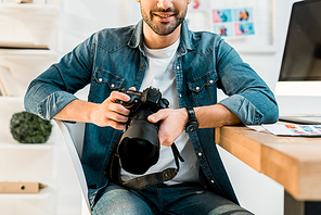 cropped shot of smiling young photographer holding camera at workplace