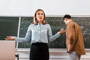 Female teacher gesturing in classroom in formalwear near student
