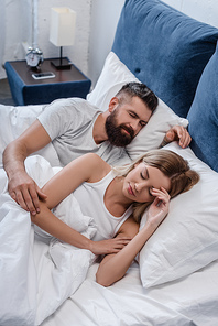 bearded young man and beautiful girl sleeping in big white bed in morning