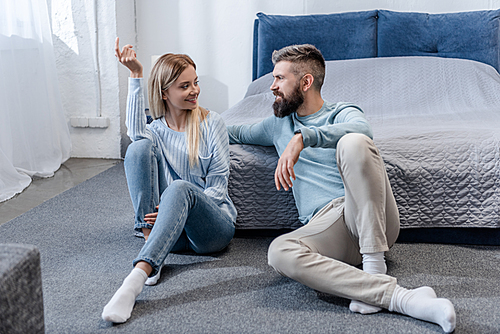 Young girl and handsome man sitting on floor and talking in blue bedroom