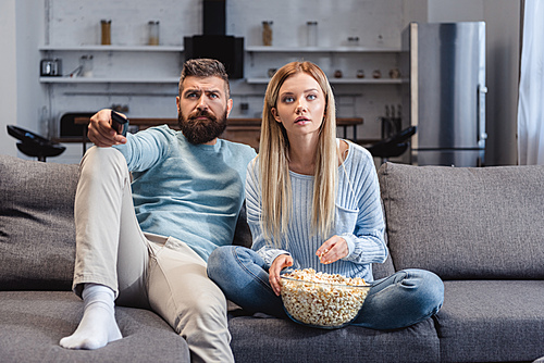 Surprised wife sitting on sofa with husband and holding popcorn