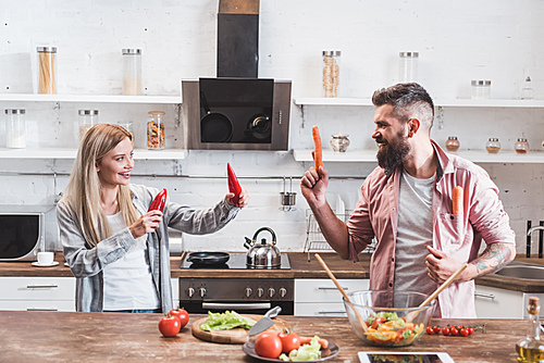 funny couple playing with vegetables while cooking dinner at wooden table