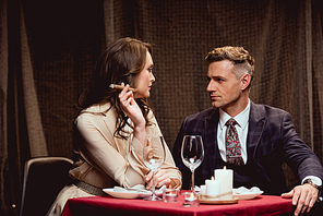 woman sitting at table and smoking cigar while having romantic dinner with handsome man in restaurant