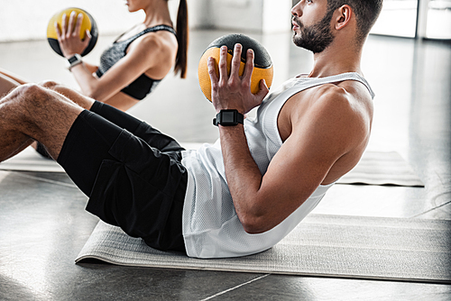 cropped shot of athletic young couple holding medicine balls and doing abs exercise on yoga mats