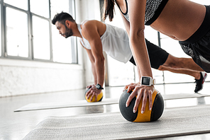 cropped shot of young sportive couple exercising with medicine balls on yoga mats