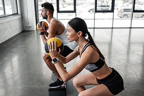 side view of athletic young man and woman holding medicine balls and exercising with step platforms in gym