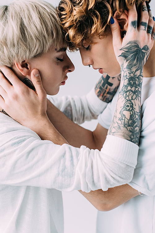 girlfriend with tattoos embracing boyfriend with curly hair isolated on grey