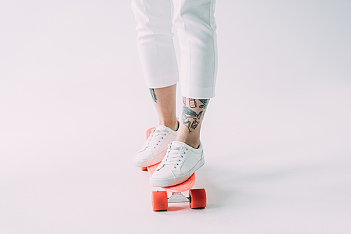 cropped view of woman riding skateboard on grey background