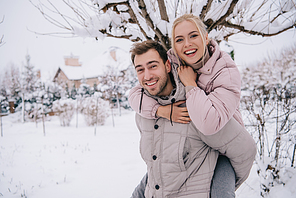 smiling man carrying attractive blonde woman on back in winter