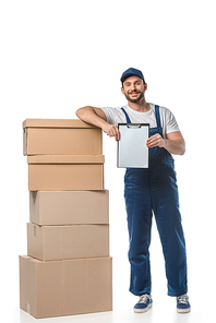 handsome mover in uniform  while holding blank clipboard near cardboard boxes isolated on white