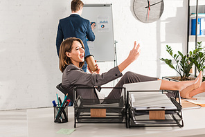 cheerful businesswoman taking selfie with paper cup near coworker in office, procrastination concept