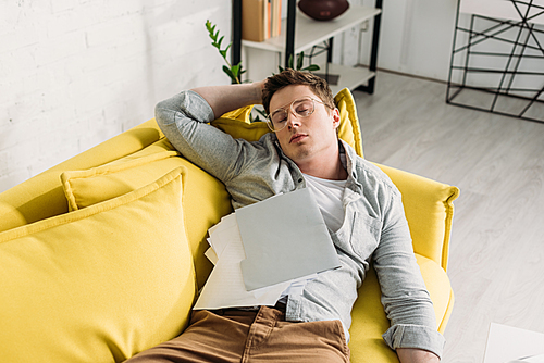 tired man sleeping on sofa with documents at home