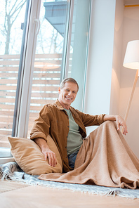 cheerful man sitting on floor by large window at new home