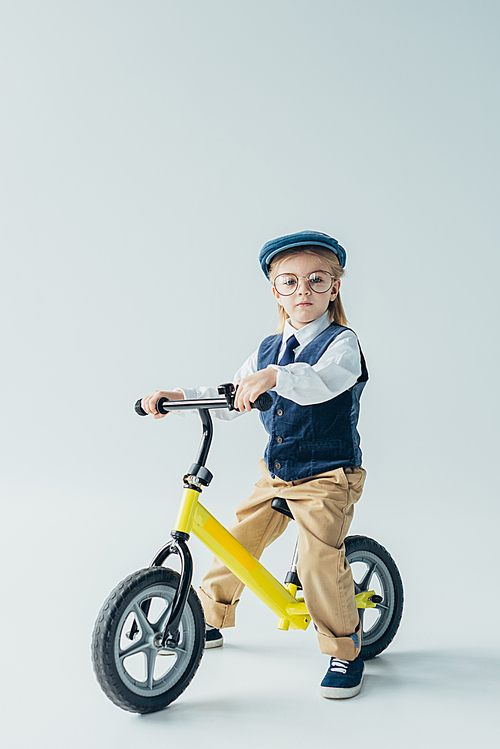 serious kid in retro vest and cap riding bike and  on grey background