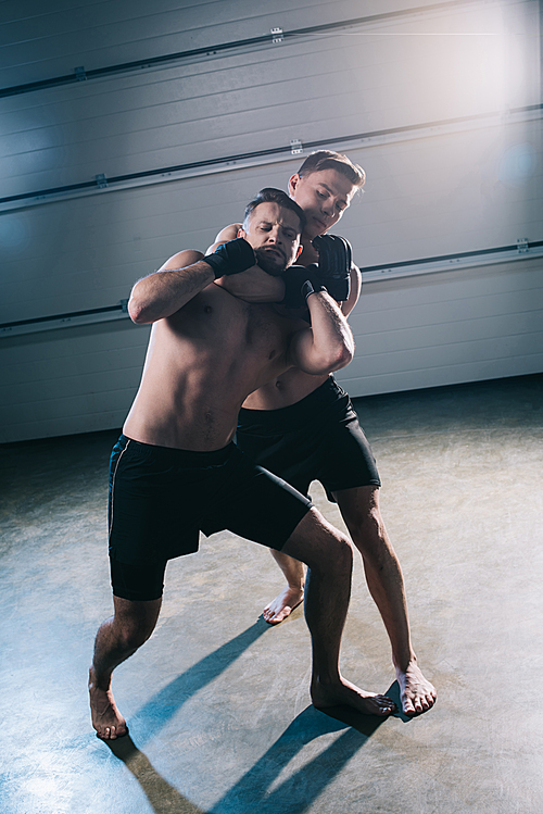 barefoot muscular mma fighter doing chokehold to sportive shirtless opponent
