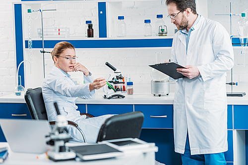 scientific researcher looking at flask with reagent in hand with colleague near by in laboratory