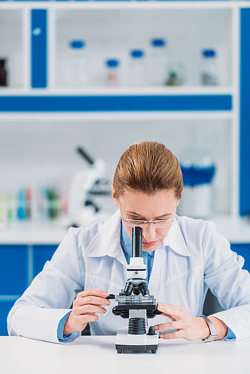 female scientist in eyeglasses looking on reagent through microscope in laboratory