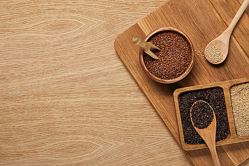 top view of white, black and red quinoa in wooden bowls on chopping board