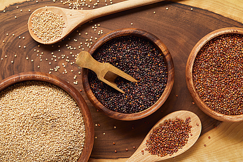 close up view of white, black and red quinoa in wooden bowls with spatula and spoons