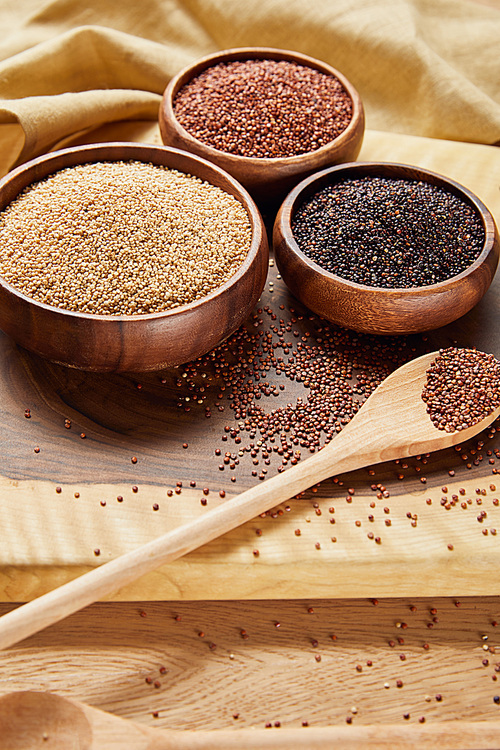 white, black and red quinoa in wooden bowls and spoon near napkin