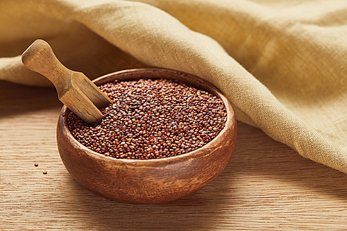 red quinoa in wooden bowl with spatula near beige napkin