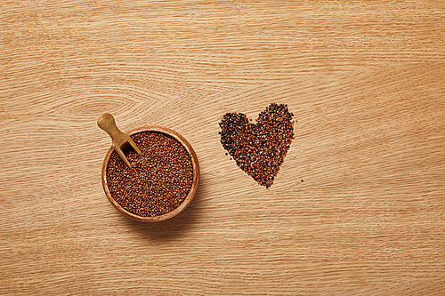 top view of red quinoa seeds in wooden bowl with spatula near heart sign