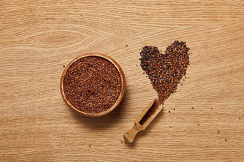 top view of red quinoa seeds in wooden bowl near heart sign and spatula