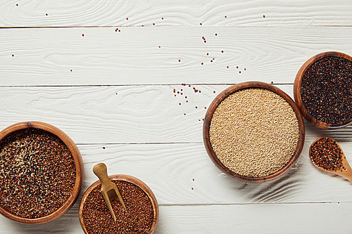 top view of white, black and red quinoa seeds in wooden bowls on white textured table