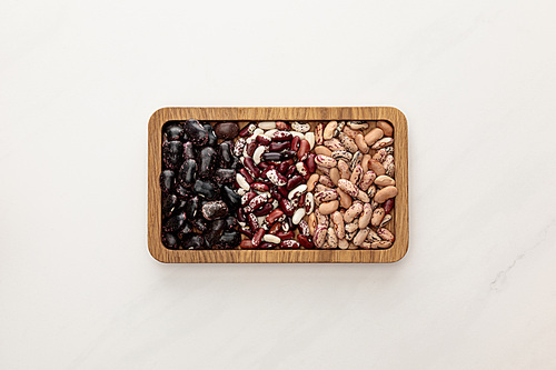top view of rectangular wooden dish with raw beans on white marble surface