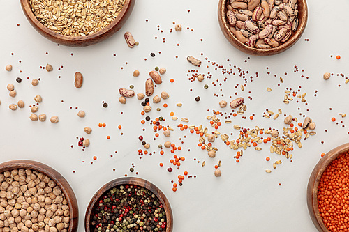top view of wooden plates with chickpea, lentil, peppercorns, oatmeal and beans near scattered grains on marble surface