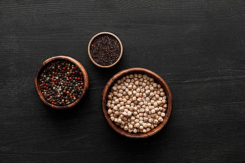 top view on brown bowls with peppercorns, black quinoa and chickpea on dark wooden surface