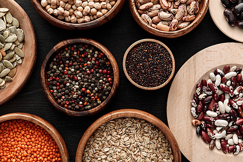 top view of diverse wooden bowls with uncooked legumes and cereals on dark surface
