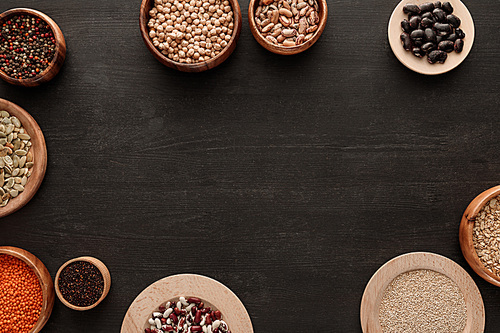 top view of legumes and cereals in bowls on dark wooden surface with copy space