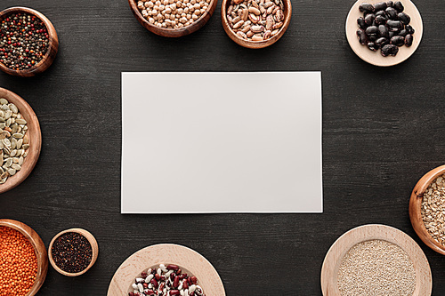 blank white paper on dark wooden surface with bowls with cereals and legumes