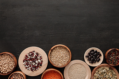 top view of raw beans, cereals, spice and pumpkin seeds in bowls on dark wooden surface with copy space