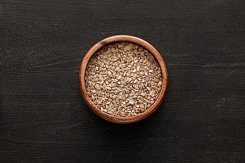 top view of brown bowl with raw oatmeal on dark wooden surface with copy space