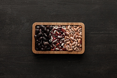 top view of rectangular brown bowl with raw assorted beans on dark wooden surface with copy space