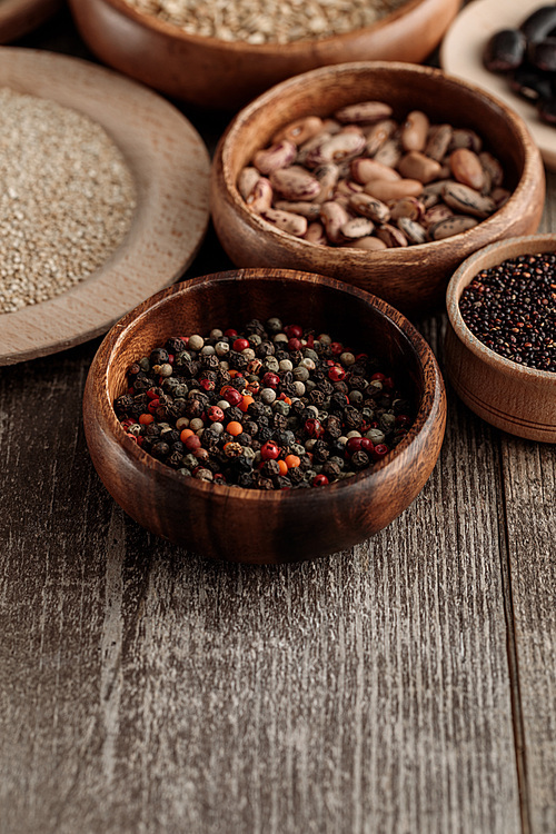 small wooden bowls with peppercorns, seeds and beans on brown table