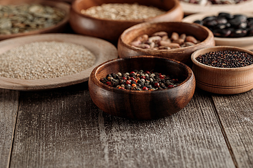 wooden bowls and plates with peppercorns, grains and beans on brown table