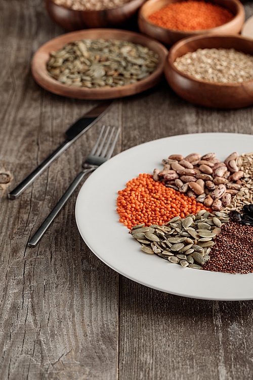 white plate with lentil, pumpkin seeds and beans near knife and fork on wooden table