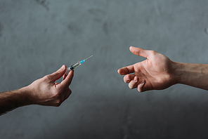 cropped shot of drug dealer giving heroin syringe to person